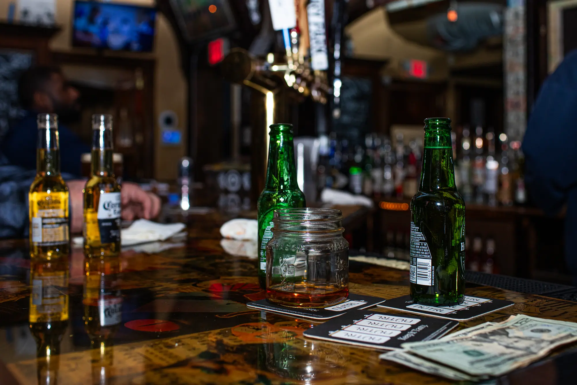 The bar top at Bond Street — bottles, a shot in a mason jar, and cash on the wood.