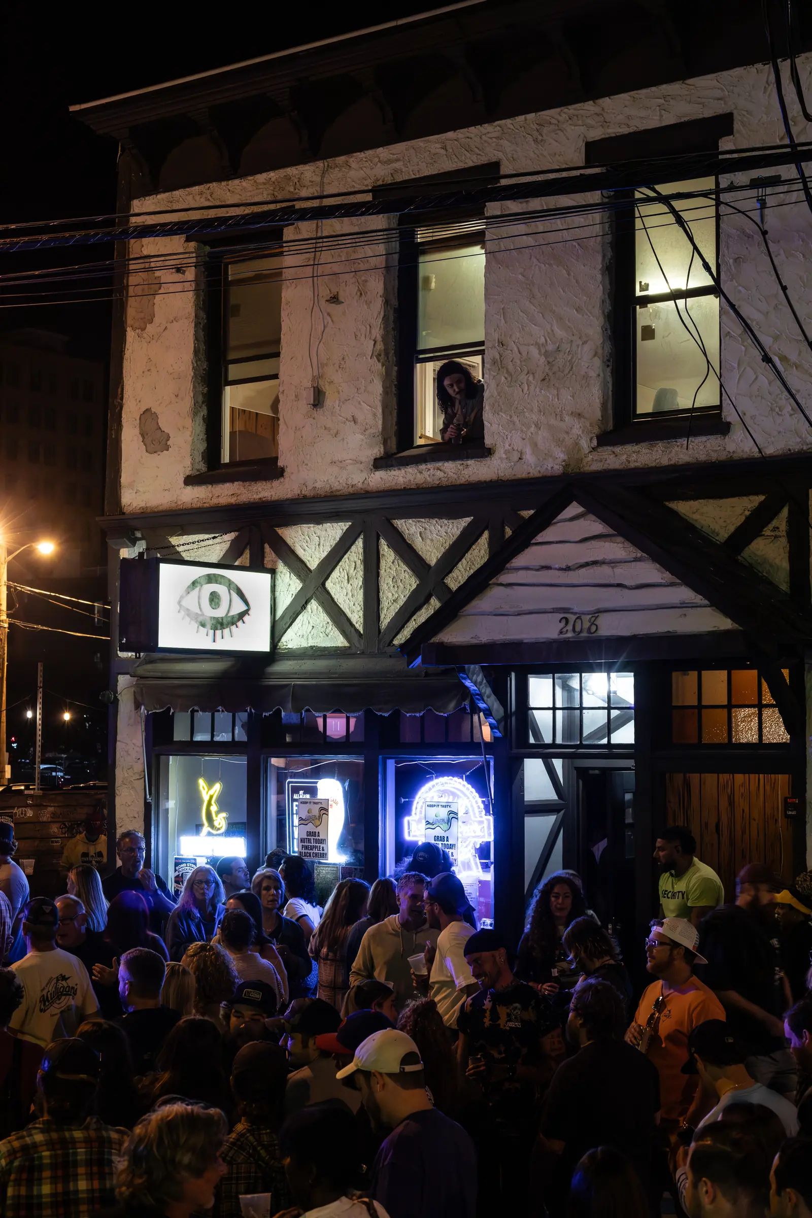 The bar lit up at night with the street full of people outside.