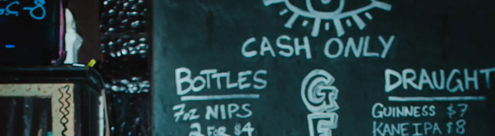 The top of the chalkboard behind the bar: the Bond Street eye, CASH ONLY, and the heads of the bottles and draught lists.