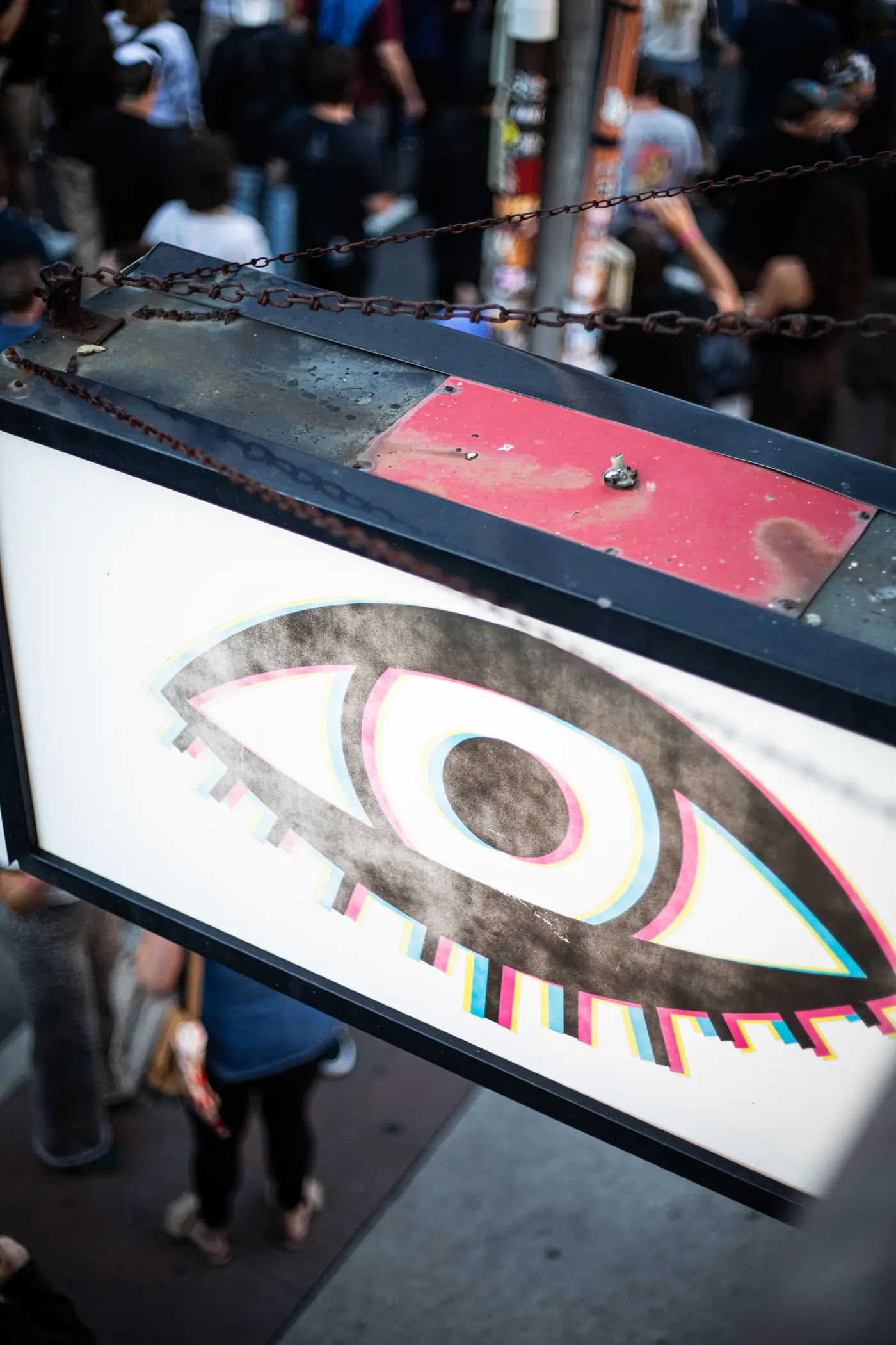 The Bond Street eye, hand-painted on a metal sign hung by chain over the sidewalk.