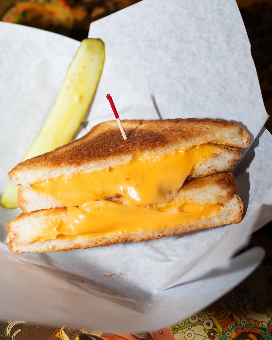 A griddled American grilled cheese cut in half on butcher paper with a pickle spear.