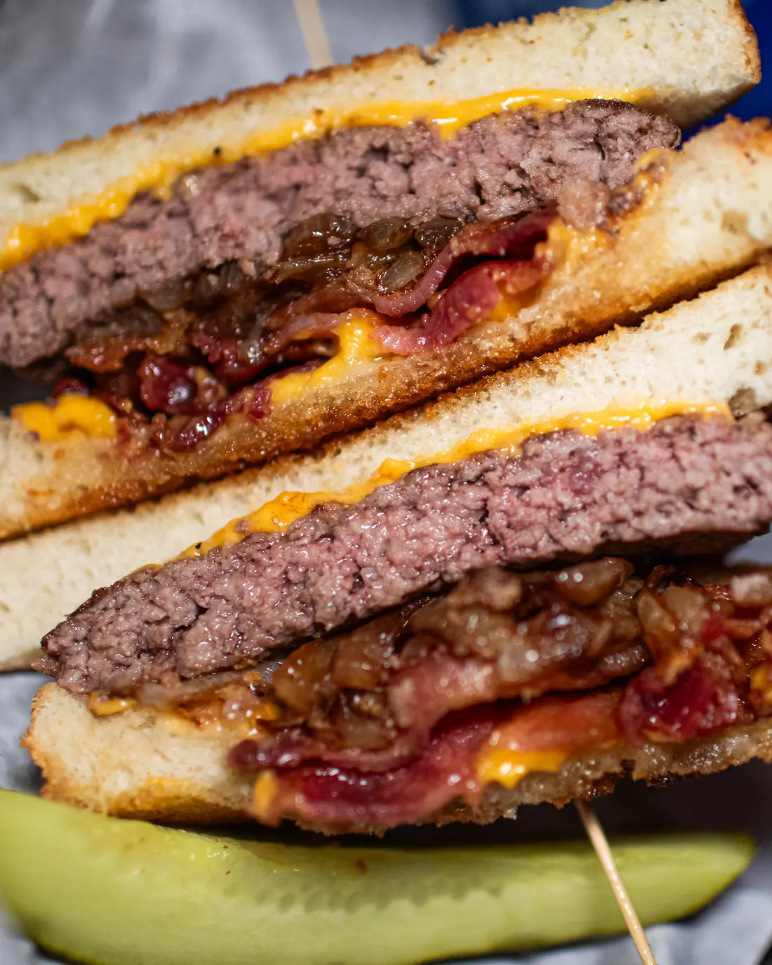 The patty melt, cut and stacked, cheese pulling, pickle spear underneath.