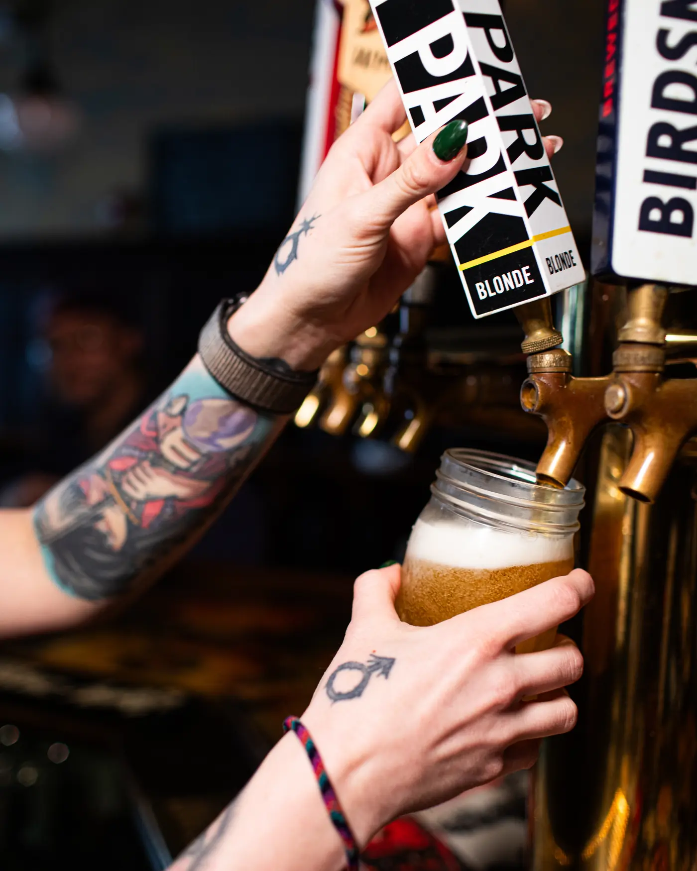 A bartender pulling the A.P. Blonde tap, filling a mason jar at the brass tower.