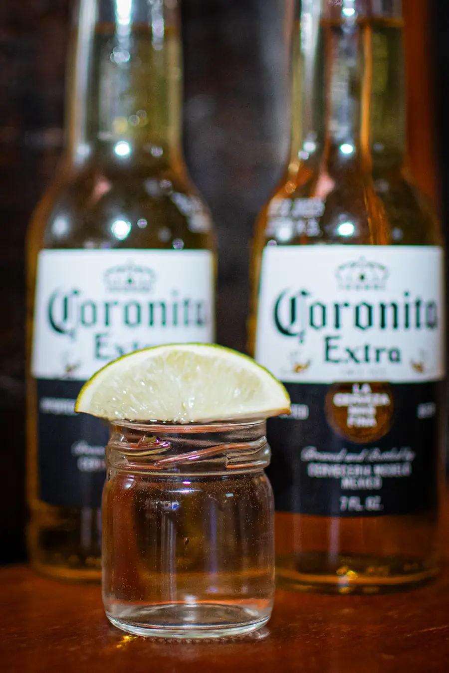 Two Coronita bottles and a lime over a shot jar.