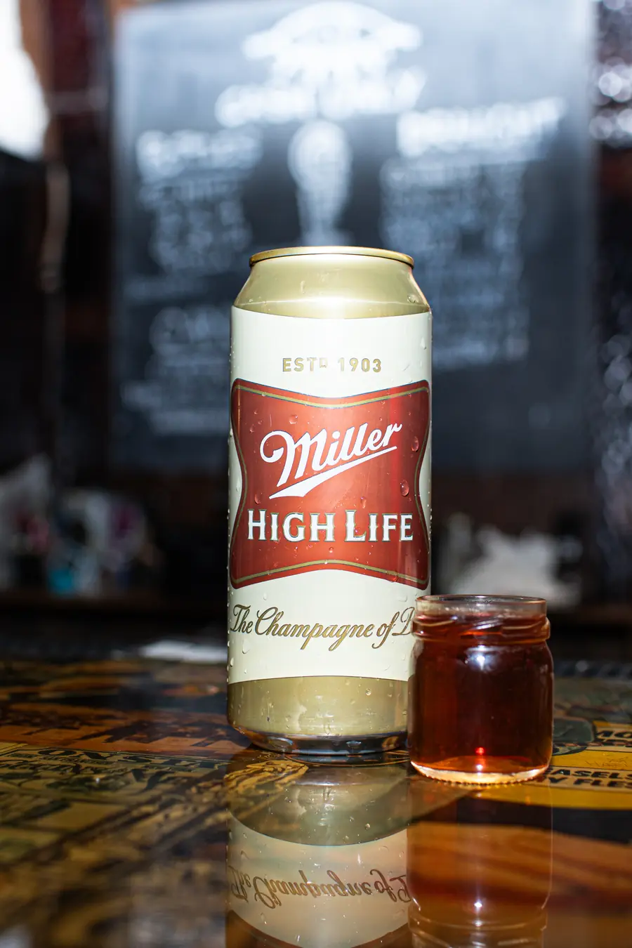 A tall Miller High Life can beside a shot in a small mason jar on the bar.